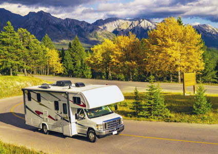 Small RV driving on the road with mountains and trees in the background